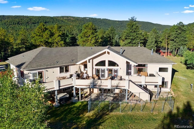 back of property featuring a fenced backyard, a shingled roof, stucco siding, and a forest view