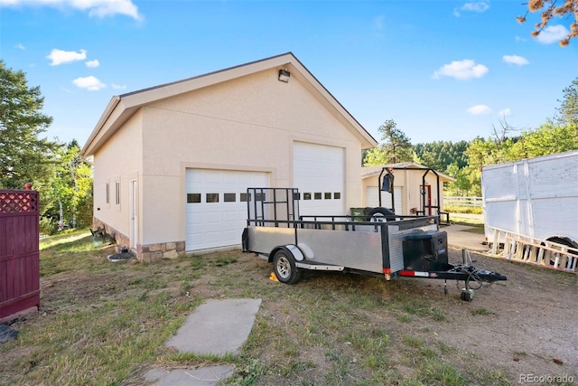 view of side of property featuring an outbuilding, stucco siding, fence, and a garage