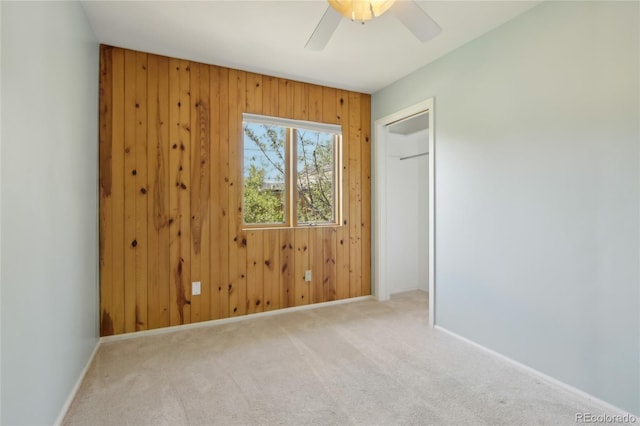unfurnished bedroom with carpet flooring, wooden walls, baseboards, a ceiling fan, and a closet