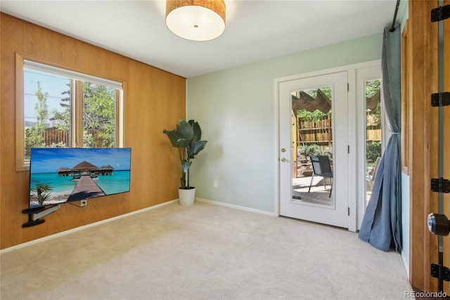 doorway to outside featuring carpet, wood walls, and baseboards