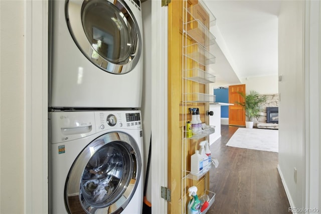 clothes washing area with stacked washer and clothes dryer, dark wood-type flooring, and baseboards