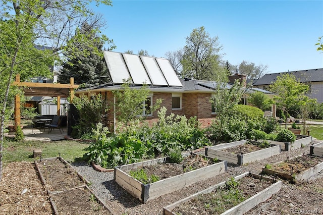 back of house with a patio, brick siding, a vegetable garden, and solar panels