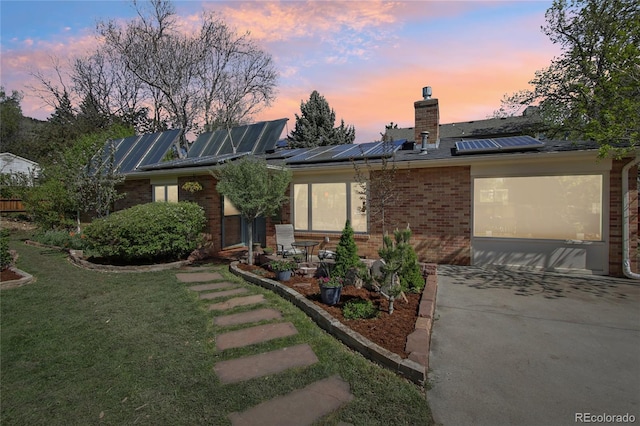 view of front facade featuring brick siding, a chimney, solar panels, and a lawn