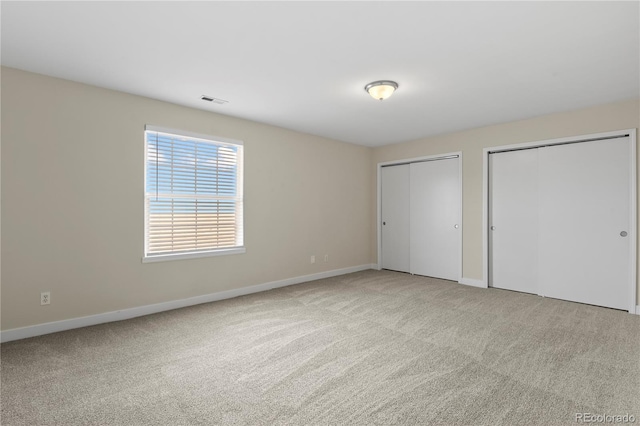 unfurnished bedroom with light carpet and multiple closets