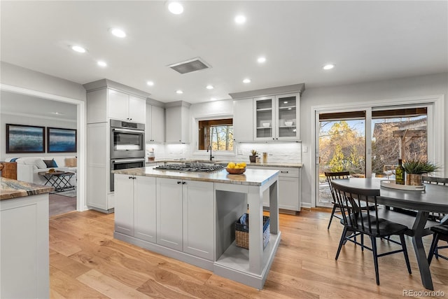 kitchen featuring stainless steel appliances, decorative backsplash, light wood-type flooring, and light stone countertops