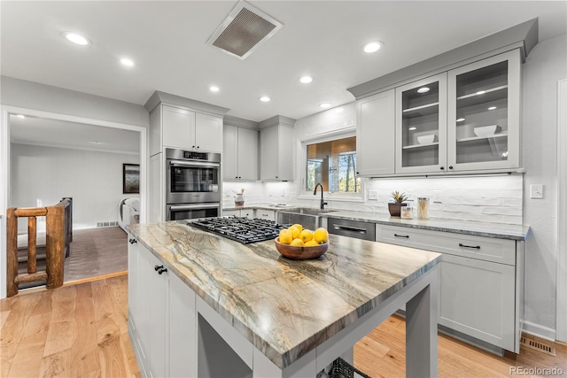 kitchen featuring light stone counters, a center island, stainless steel appliances, light hardwood / wood-style floors, and sink