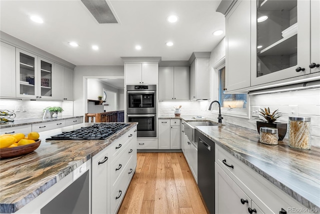 kitchen featuring sink, white cabinetry, light stone counters, light hardwood / wood-style flooring, and appliances with stainless steel finishes