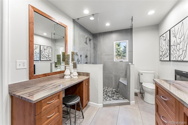 bathroom with tiled shower, tile patterned flooring, vanity, and toilet