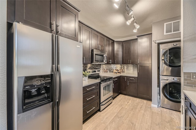 kitchen with stainless steel appliances, stacked washer / drying machine, dark brown cabinets, backsplash, and light wood finished floors