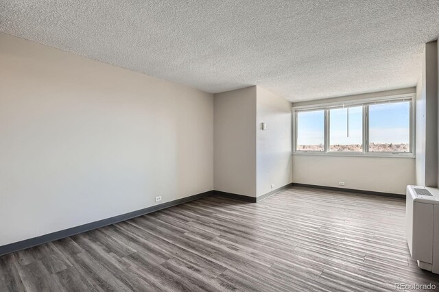 2225 Buchtel Blvd Unit 1003, Denver, CO 80210 - empty room featuring baseboards, a textured ceiling, radiator heating unit, and wood finished floors
