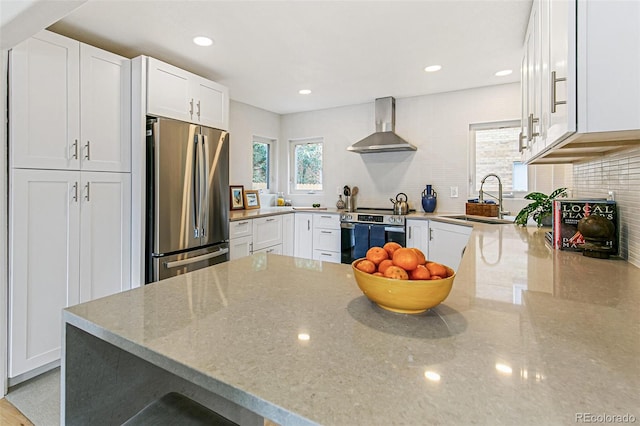 kitchen featuring decorative backsplash, white cabinets, sink, stainless steel appliances, and wall chimney exhaust hood