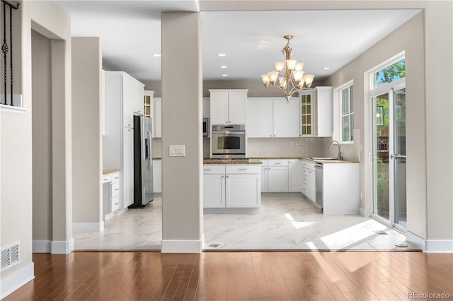 23870 E Dorado Pl, Aurora, CO 80016 - kitchen featuring appliances with stainless steel finishes, a chandelier, glass insert cabinets, a sink, and white cabinetry