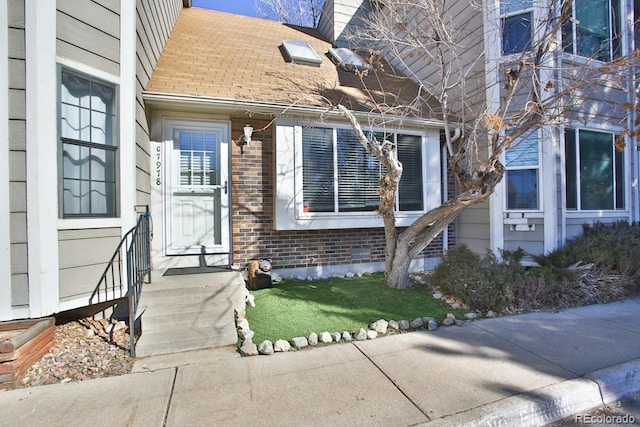 doorway to property with brick siding and a shingled roof