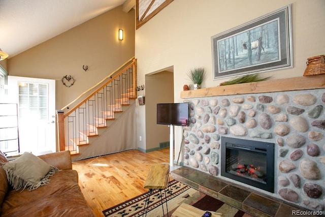 living area with visible vents, wood finished floors, stairs, a stone fireplace, and high vaulted ceiling