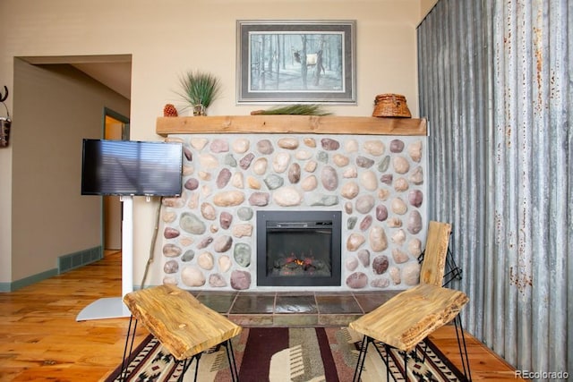 room details with a stone fireplace, wood finished floors, visible vents, and baseboards