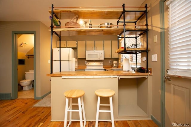 kitchen with a peninsula, white appliances, baseboards, wooden counters, and light wood-type flooring