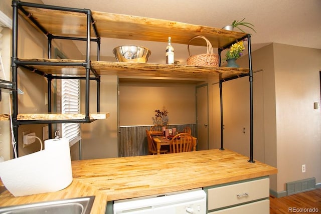 interior space with dishwasher, wood finished floors, wood counters, and visible vents