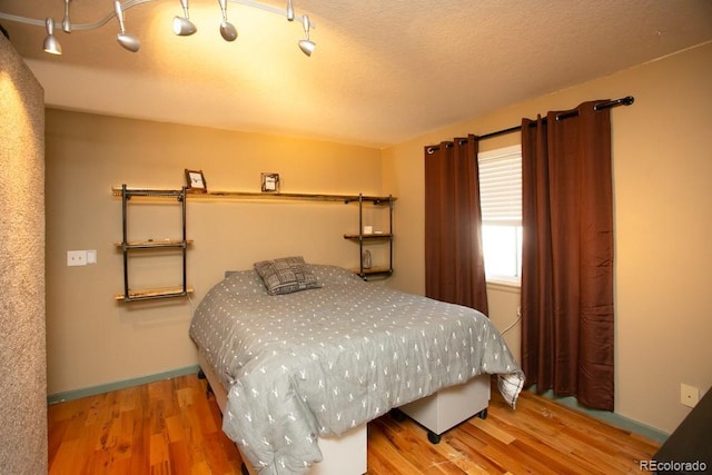 bedroom featuring a textured ceiling, wood finished floors, and baseboards