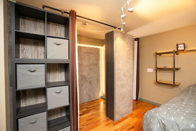 bedroom with rail lighting, a textured ceiling, baseboards, and wood finished floors