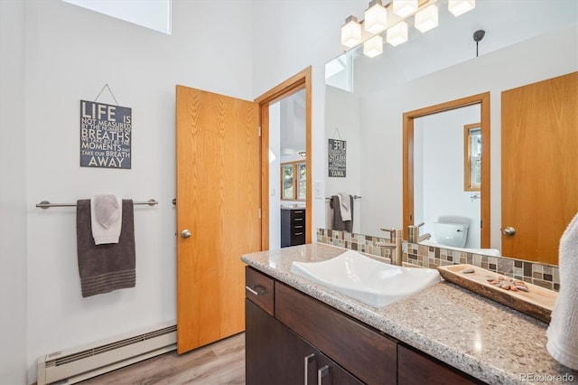 7350 Timber Trail Rd, Evergreen, CO 80439 - bathroom featuring a baseboard radiator, wood finished floors, vanity, decorative backsplash, and a towering ceiling
