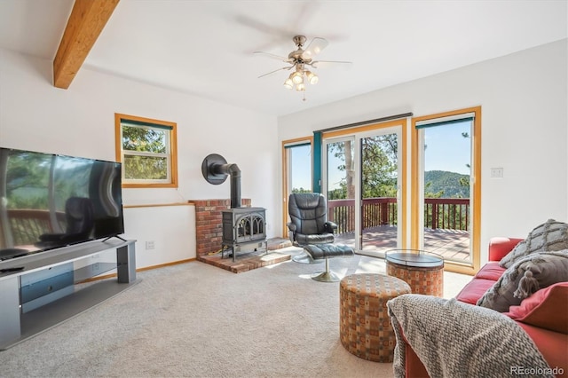 7350 Timber Trail Rd, Evergreen, CO 80439 - living room with a wood stove, plenty of natural light, ceiling fan, carpet flooring, and beam ceiling