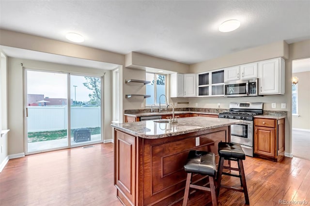 12047 W Coal Mine Dr, Littleton, CO 80127 - kitchen with stainless steel appliances, open shelves, a kitchen island with sink, light wood finished floors, and baseboards