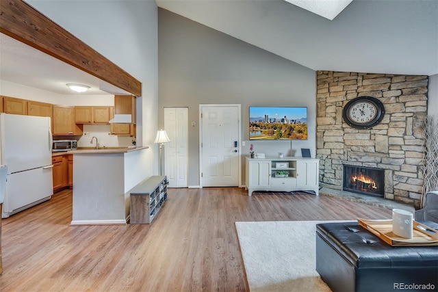 unfurnished living room featuring sink, light wood-type flooring, a fireplace, beamed ceiling, and high vaulted ceiling