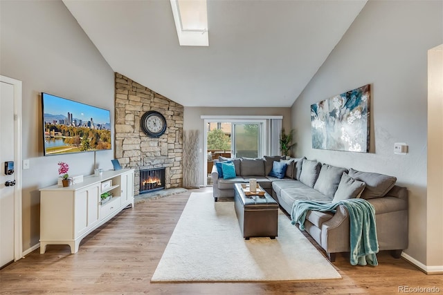 living room featuring a skylight, high vaulted ceiling, a fireplace, and light hardwood / wood-style flooring