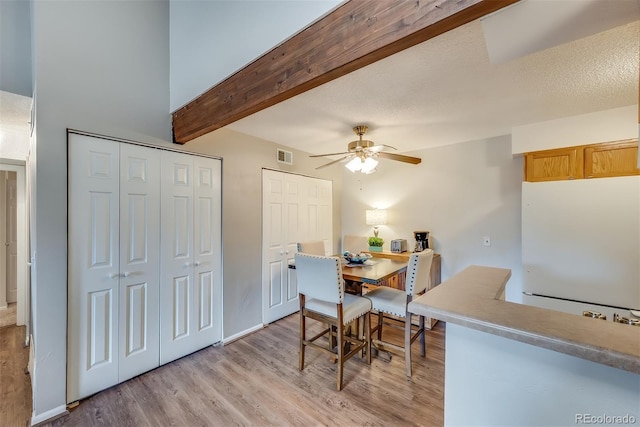 dining room with ceiling fan, beam ceiling, light hardwood / wood-style floors, and a textured ceiling