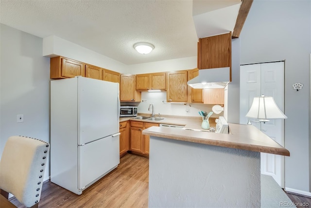 kitchen featuring sink, wall chimney range hood, light hardwood / wood-style flooring, white refrigerator, and kitchen peninsula