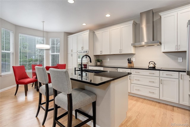 24686 E Florida Ave, Aurora, CO 80018 - kitchen featuring wall chimney range hood, a sink, a breakfast bar, light wood finished floors, and dark countertops