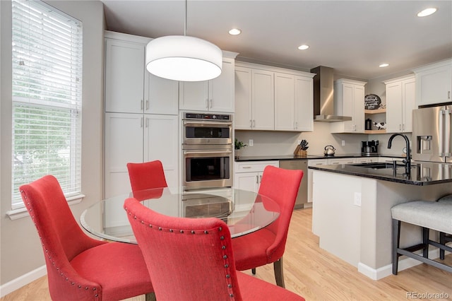 24686 E Florida Ave, Aurora, CO 80018 - kitchen with wall chimney range hood, appliances with stainless steel finishes, a sink, dark countertops, and light wood-style flooring