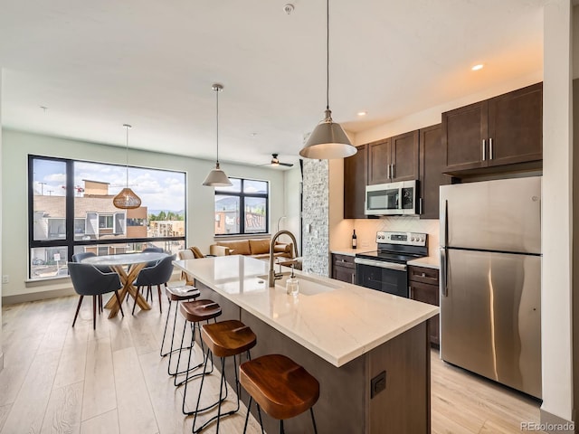 75 W 4th St Unit 205W, Silverthorne, CO 80498 - kitchen with stainless steel appliances, dark brown cabinetry, decorative backsplash, light wood-type flooring, and a kitchen breakfast bar