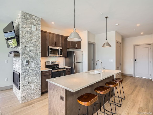 75 W 4th St Unit 205W, Silverthorne, CO 80498 - kitchen featuring appliances with stainless steel finishes, light wood-style floors, dark brown cabinets, a kitchen bar, and an island with sink