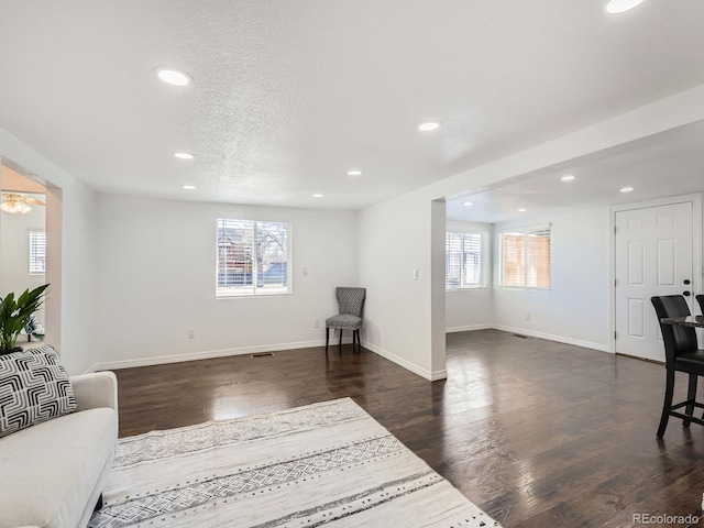 living area featuring a healthy amount of sunlight, a textured ceiling, baseboards, and dark wood-type flooring