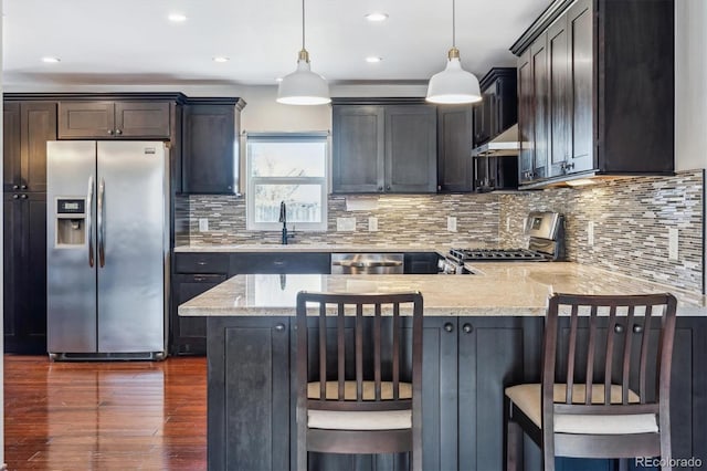 kitchen featuring under cabinet range hood, tasteful backsplash, appliances with stainless steel finishes, a peninsula, and hanging light fixtures