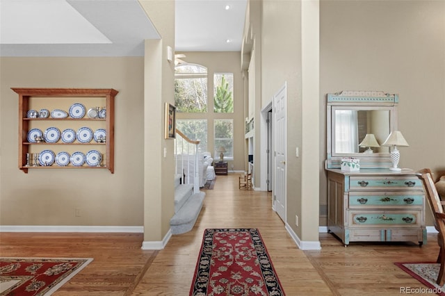 hallway featuring stairway, light wood-style floors, baseboards, and a towering ceiling