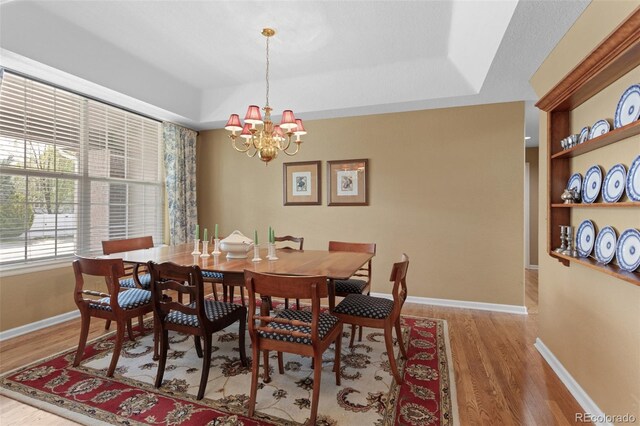 dining area with wood finished floors, a chandelier, baseboards, and a raised ceiling