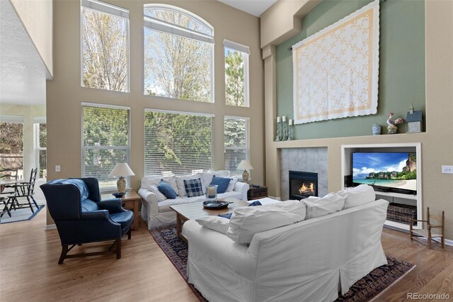 living area featuring plenty of natural light, a tile fireplace, wood finished floors, and a high ceiling