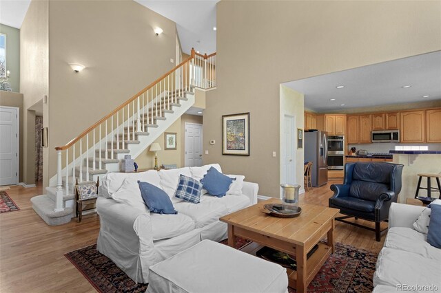 living room with a towering ceiling, stairway, light wood finished floors, and recessed lighting