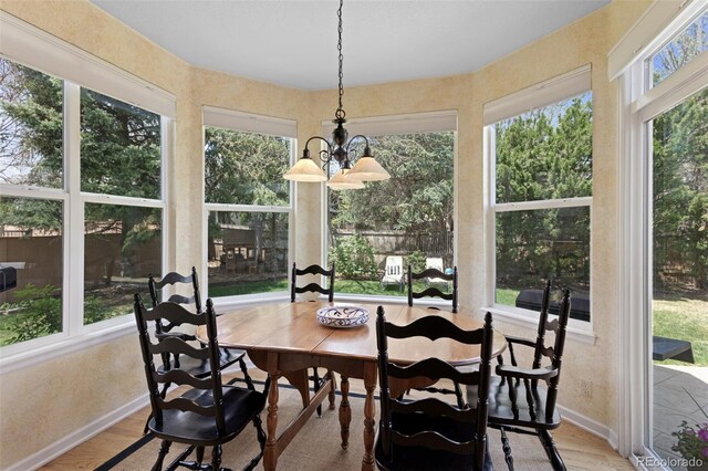 sunroom / solarium featuring wood finished floors, a chandelier, and baseboards