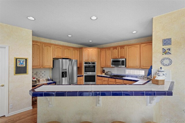 kitchen with stainless steel appliances, a breakfast bar, a peninsula, tile counters, and light wood finished floors