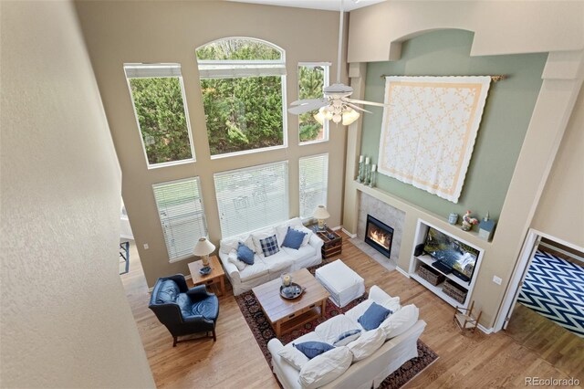 living room with a ceiling fan, a tile fireplace, wood finished floors, and a high ceiling