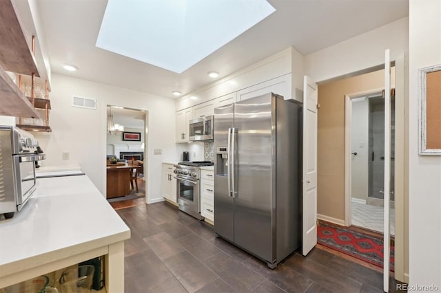 kitchen featuring stainless steel appliances, white cabinetry, and a skylight