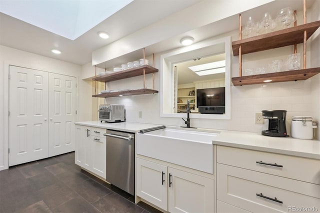 kitchen featuring tasteful backsplash, a skylight, white cabinetry, stainless steel dishwasher, and sink