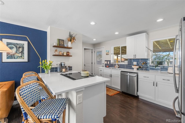 kitchen featuring stainless steel dishwasher, black electric cooktop, a peninsula, dark wood-style flooring, and white cabinets