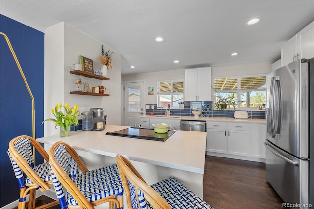 kitchen featuring appliances with stainless steel finishes, a peninsula, a kitchen breakfast bar, tasteful backsplash, and dark wood-style floors