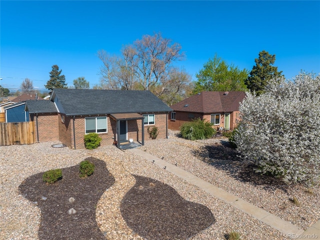 ranch-style house featuring brick siding, fence, and roof with shingles