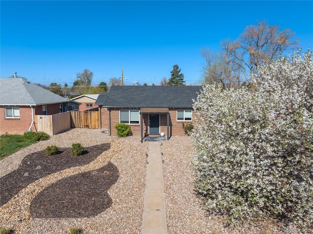 view of front of home featuring fence, brick siding, and a shingled roof