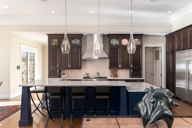 kitchen featuring dark brown cabinets, wall chimney range hood, and built in refrigerator